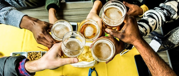 Foto mãos cortadas de amigos brindando com copos de cerveja no bar.