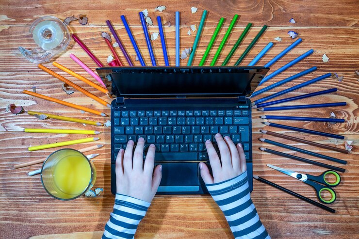 Foto mãos cortadas de criança usando laptop por lápis coloridos na mesa