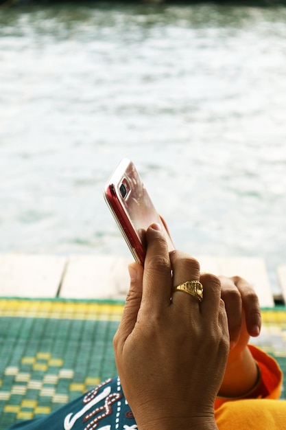 Mãos cortadas de homem usando telefone móvel contra o lago