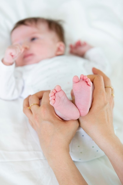 Mãos cortadas de mãe segurando as pernas da filha na cama