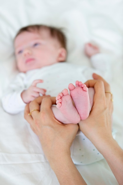 Mãos cortadas de mãe segurando as pernas da filha na cama