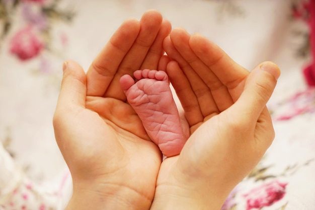 Mãos cortadas de mãe segurando o pé do bebê na cama