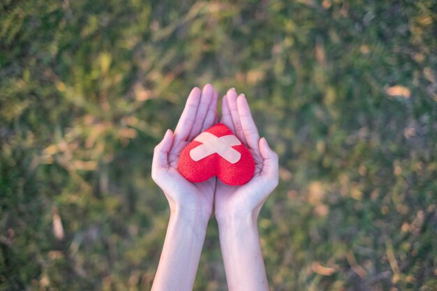 Foto mãos cortadas de mulher segurando forma de coração vermelho com decoração de bandagens em terra