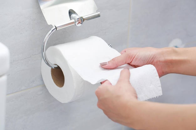 Mãos cortadas de mulher segurando papel higiênico no banheiro