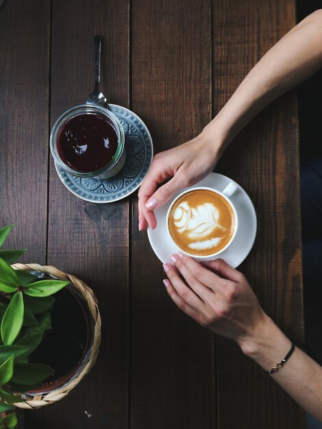 Mãos cortadas de mulher segurando xícara de café na mesa