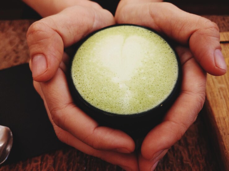 Foto mãos cortadas de pessoa segurando xícara com chá matcha na mesa