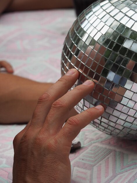 Foto mãos cortadas de pessoa tocando bola de discoteca na cama