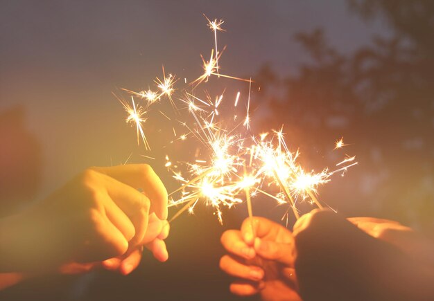 Foto mãos cortadas de pessoas segurando faíscas iluminadas à noite