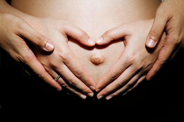 Mãos cortadas de um casal tocando a barriga contra um fundo preto