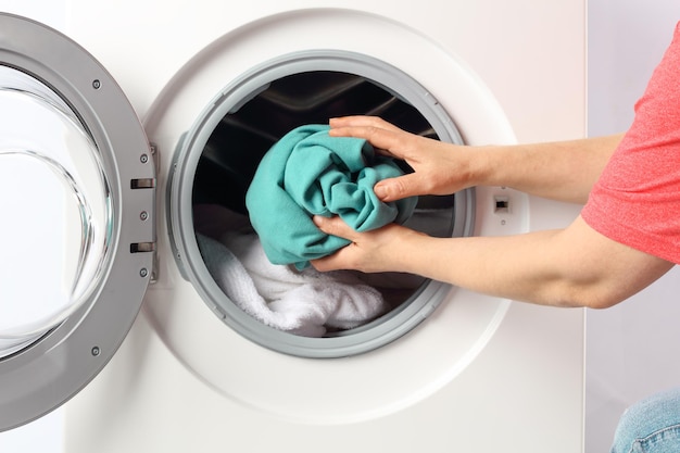Mãos cortadas de um homem colocando roupas na máquina de lavar em casa