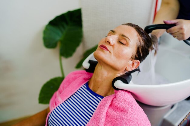 Foto mãos cortadas de uma esteticista a lavar o cabelo no salão.