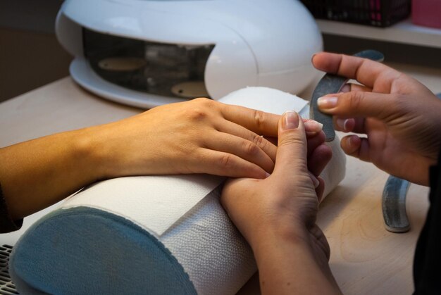 Mãos cortadas de uma esteticista aplicando arte de unhas a um cliente