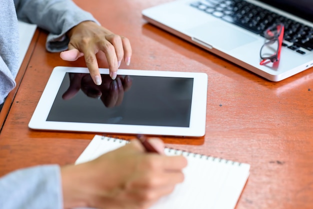 Mãos cortadas de uma mulher de negócios usando um tablet digital enquanto escrevia no escritório