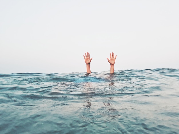 Mãos cortadas de uma pessoa emergindo do mar contra um céu claro