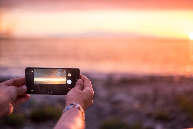 Foto mãos cortadas fotografando o mar com um smartphone ao pôr-do-sol