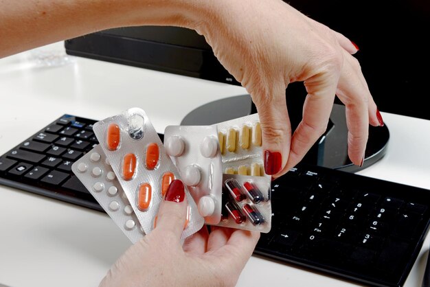 Foto mãos cortadas segurando vários medicamentos sobre o teclado