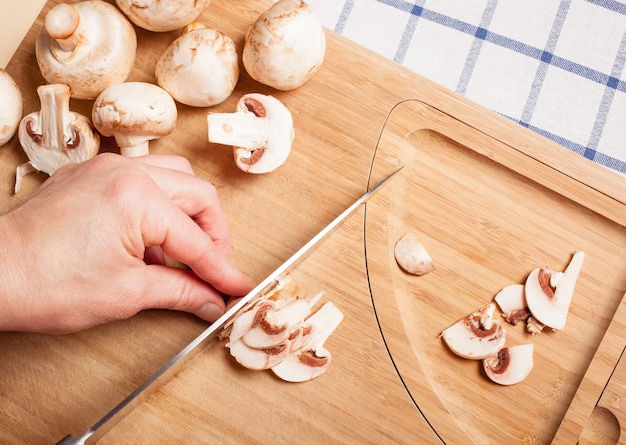 Mãos cortando champignon em uma placa de madeira