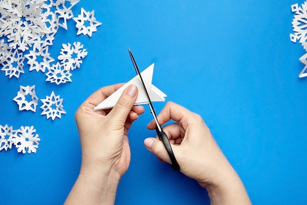 Mãos cortando flocos de neve de papel branco em azul