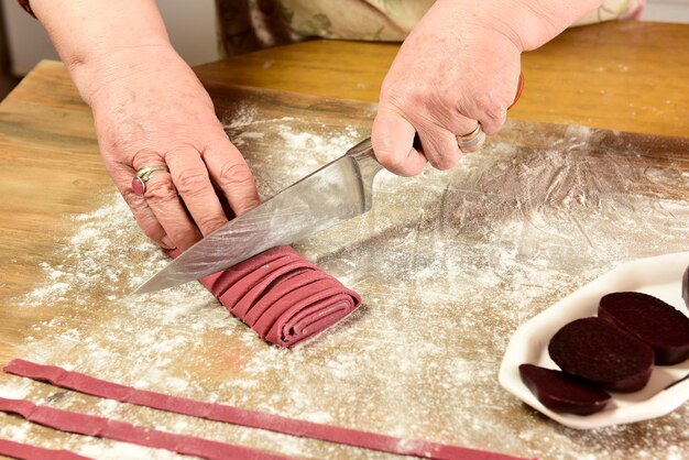 Mãos cortando macarrão roxo com ingredientes na mesa comida italiana caseira