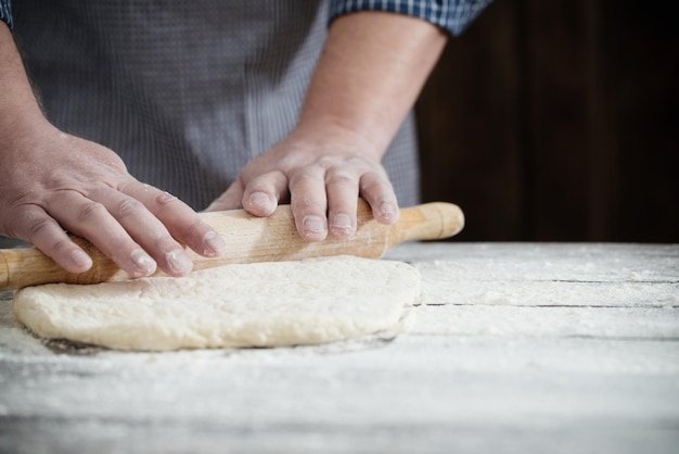 Mãos cozinhando massa no fundo escuro de madeira