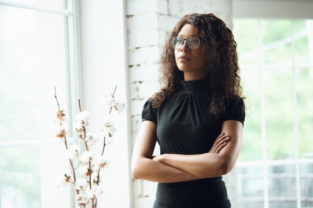 Mãos cruzadas. Mulher de negócios afro-americana em traje de escritório sorrindo, parece confiante e séria, ocupada. Conceito de finanças, negócios, igualdade e direitos humanos. Bela jovem modelo, bem-sucedida.