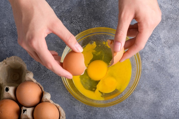 Mãos da dona de casa quebrando gema de ovo fresca e branco caindo em uma tigela vista superior