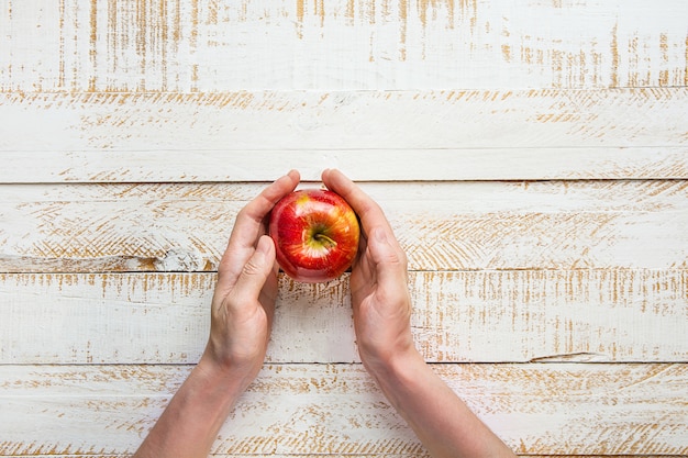 Mãos da jovem mulher que guardam apple vermelho maduro na tabela branca da madeira da prancha. ação de graças