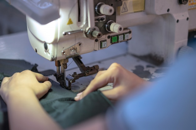 Mãos da mulher asiática nova que usa a máquina de costura na oficina.