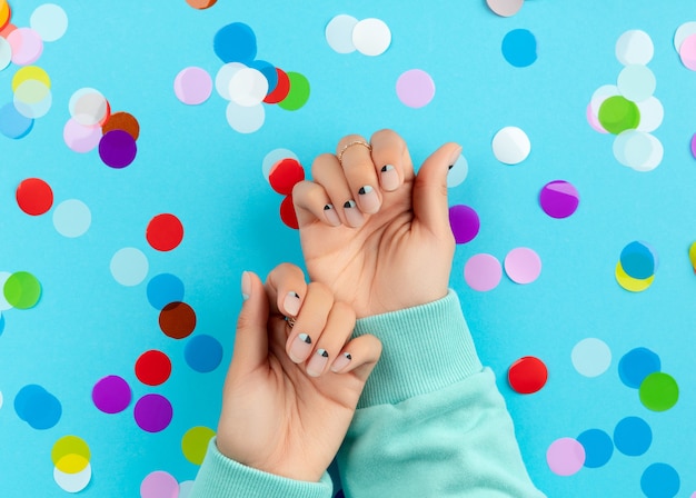 Mãos da mulher com confetes coloridos sobre fundo azul. Conceito de salão de beleza, moda e spa