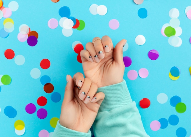 Mãos da mulher com confetes coloridos sobre fundo azul. conceito de salão de beleza, moda e spa