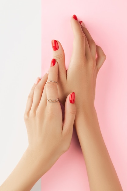 Foto mãos da mulher com manicure vermelha na moda sobre fundo branco e rosa