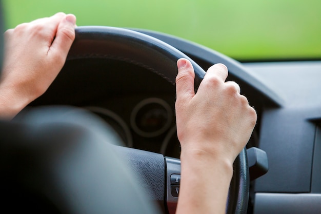 Mãos da mulher no volante que conduz um carro.