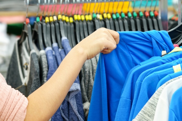 Mãos da mulher que escolhe a roupa azul na alameda da forma.