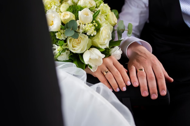 Mãos da noiva e do noivo com anéis e buquê de flores