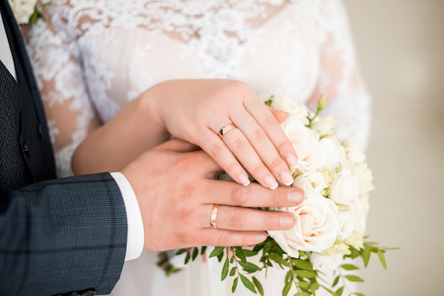 Mãos da noiva e do noivo com anéis no buquê de casamento. conceito de casamento.