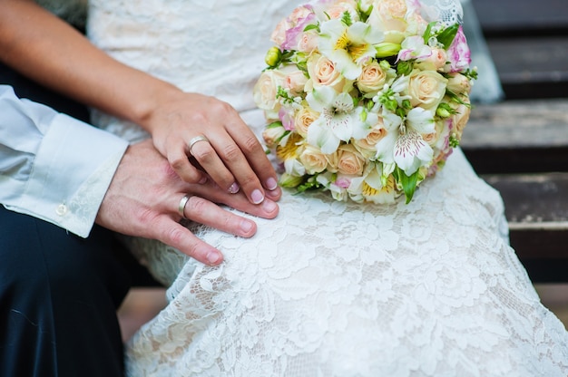 Mãos da noiva e do noivo com anéis no buquê de casamento.