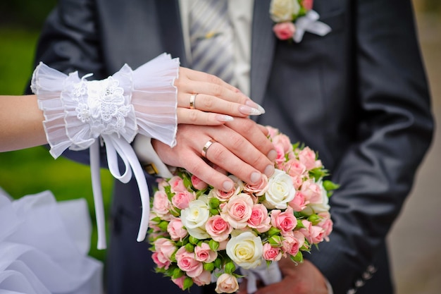 Mãos da noiva e do noivo com anéis no buquê de casamento