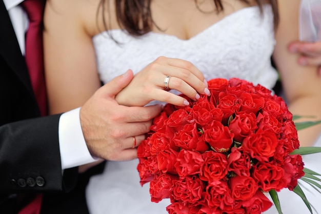 Foto mãos da noiva e do noivo com anéis no buquê de casamento