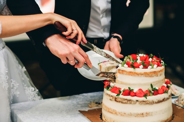 mãos da noiva e do noivo cortando o bolo de casamento