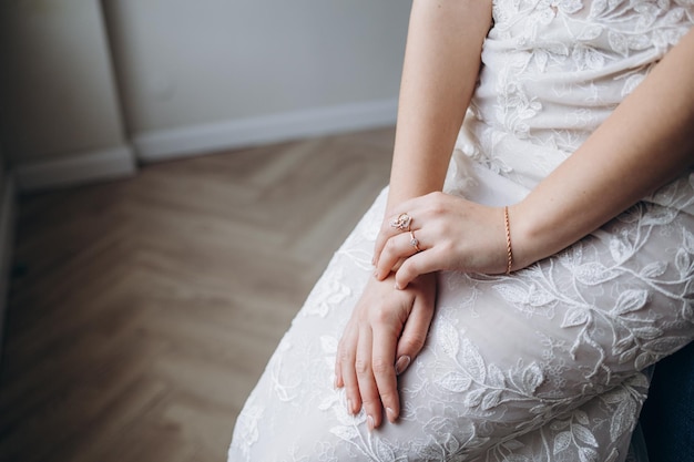 Mãos da noiva em um vestido de noiva branco com um anel de noivado de ouro com um diamante fechado A noiva toca o anel com os dedos