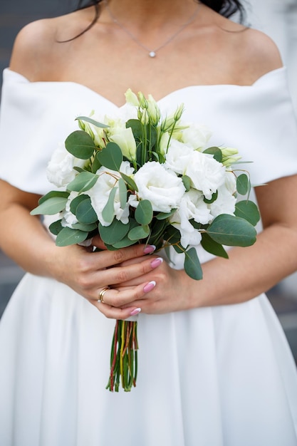 Mãos da noiva fechadas com um buquê de lindas flores frescas Atributo da noiva
