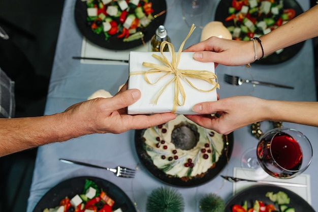 Foto mãos dando um presente de gravata-borboleta em uma caixa sobre uma mesa de jantar de natal. vista do topo.