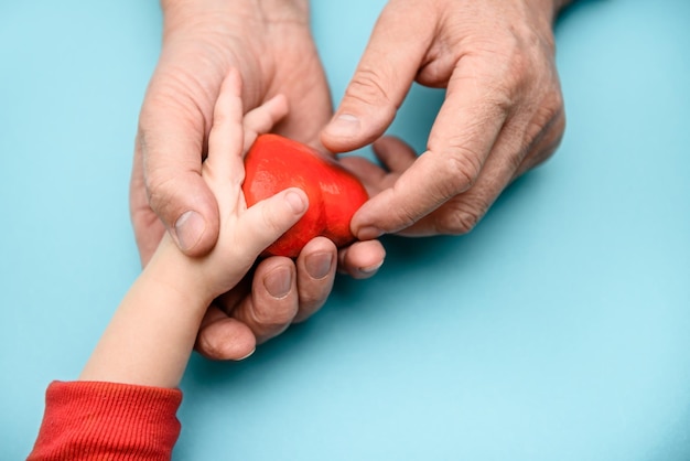 Mãos de adultos e crianças segurando um coração vermelho o conceito de amor de saúde e família dia das mães dia da saúde