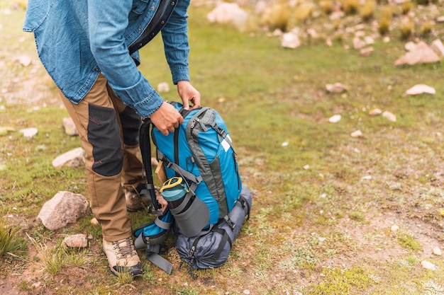 mãos de alpinista desembalando mochila de caminhada azul na montanha cercada por vegetação verde