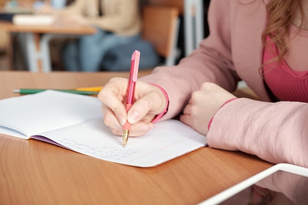 Mãos de aluna fazendo anotações no caderno durante a aula