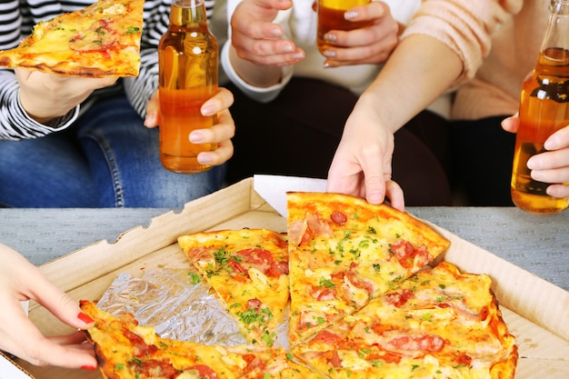 Mãos de amigos com garrafas de cerveja e pizza, close-up