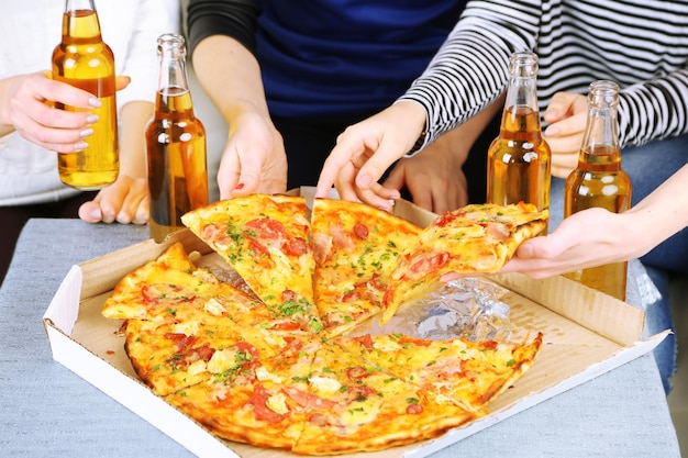 Mãos de amigos com garrafas de cerveja e pizza fecham