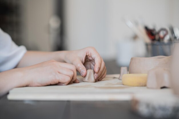 Mãos de artesão conectam as peças de barro feitas de barro bruto dedos de mestre trabalham com pedaços de barro mulher senta-se em uma oficina atrás da mesa