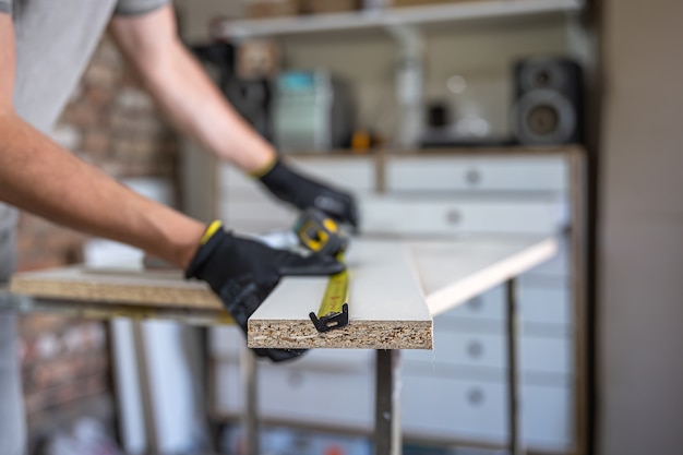 Mãos de artesão usando fita métrica e lápis para fazer marcas no pedaço de madeira colocado.