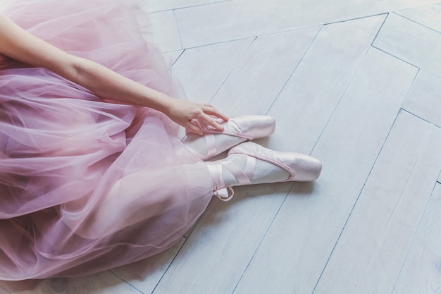 Mãos de bailarina com saia tutu rosa calçam sapatilhas de ponta na perna no corredor de luz branca
